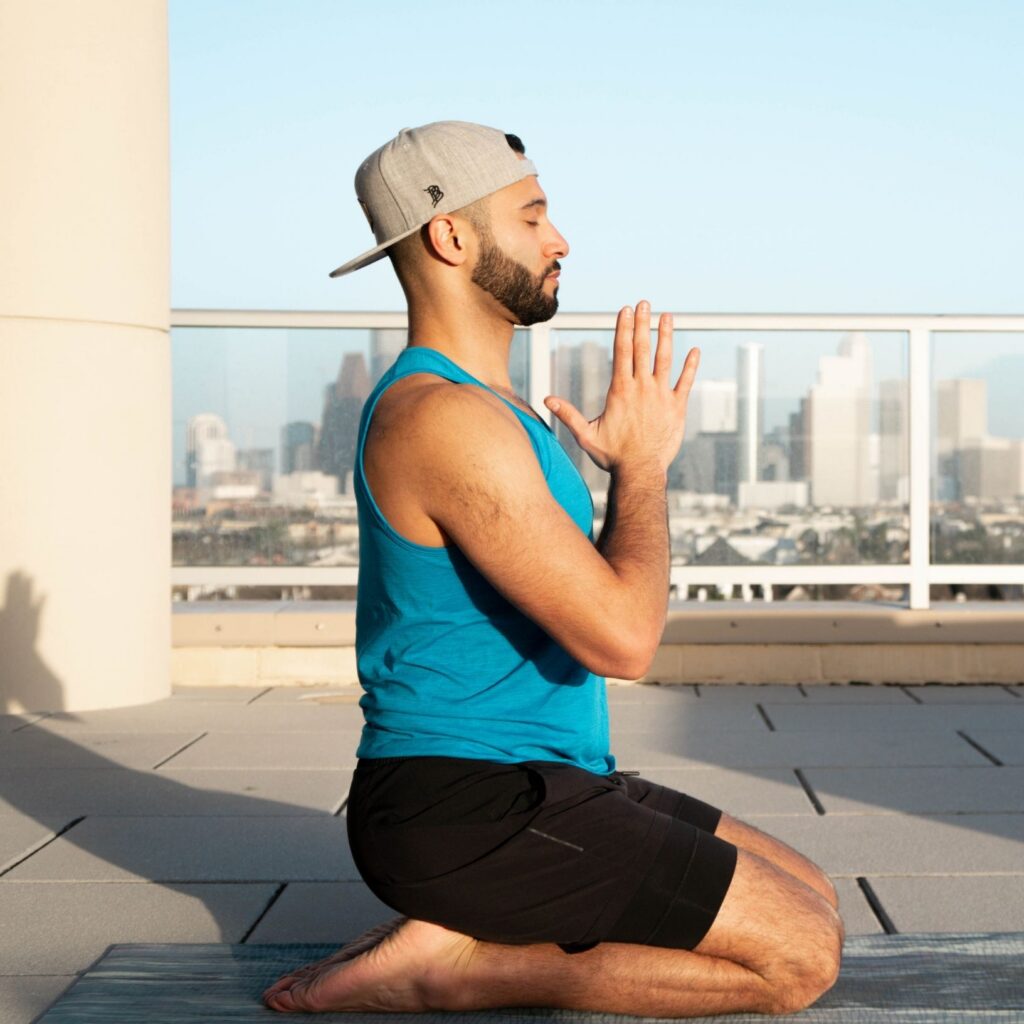 Coach John Marshall meditating in a hero's pose on a yoga mat in front of the city of Houston's skyline.
